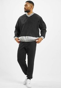 Cazadora negra con un dobladillo elástico gris y cuello a rayas, combinada con pantalones de chándal negros y zapatillas blancas. Textura suave, corte relajado.
