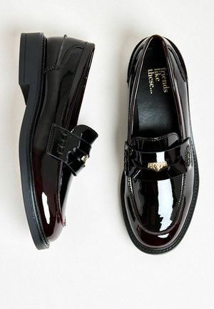 Schwarze Lackleder-Lederschuhe mit glänzender Oberfläche, ausgestattet mit einem dekorativen Riemen und goldfarbenen Beschlägen. Niedriger Blockabsatz, glatte Textur.
