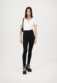 Witte geribbelde top met korte mouwen en een sleutelgaatje-detail, gecombineerd met high-waisted zwarte skinny jeans en zwarte chunky platform schoenen.