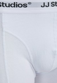 Weiße Baumwoll-Boxershorts mit einem elastischen Bund, der das schwarze "JJ Studios"-Logo zeigt, glatter Textur und kontrastierenden Nähdetails.