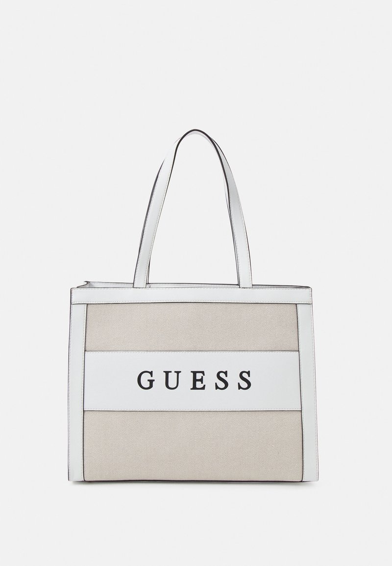 Torba na ramię z beżowego materiału z białymi akcentami. Posiada dwa paski na ramię oraz wyraźne czarne logo "GUESS" z przodu.