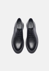 Black leather shoes with a textured finish, rounded toe, thin laces, and a flat sole. Branding visible on the insole.