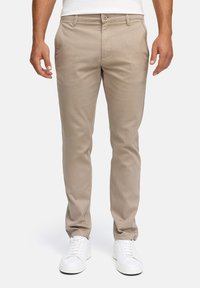 Beige katoenen chinos met een slanke pasvorm, uitgerust met een ritssluiting en zakken aan de voorkant. Gecombineerd met witte sneakers voor een frisse uitstraling.