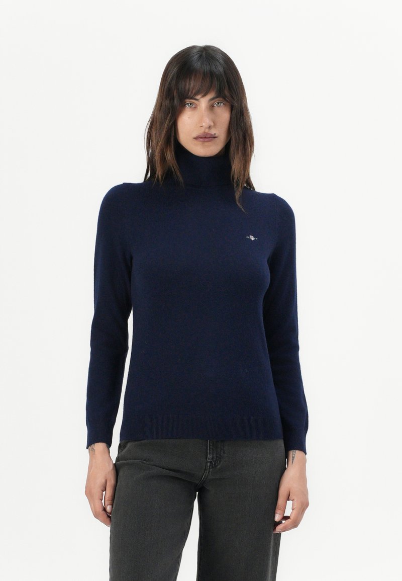 Marineblauer Rollkragenpullover aus weichem, glattem Strickstoff. Hat lange Ärmel und eine taillierte Passform mit einem kleinen Logo auf der Brust.