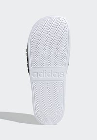 Sorte og hvite Adidas-såler med et strukturert fiskebensmønster, hvor merkevaren er tydelig og med avrundede kanter for fleksibilitet.
