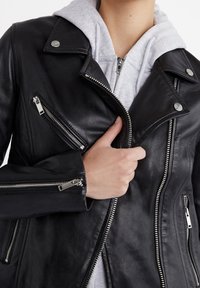 Schwarze Leder-Motorradjacke mit silbernen Reißverschlüssen und Druckknöpfen. Verfügt über mehrere Reißverschlusstaschen und ein tailliertes Design.