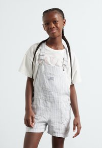 Stripete denim overall med justerbare stropper og frontlomme, paret med en enkel hvit T-skjorte med rosa tekst.