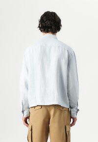 Light blue striped shirt with a relaxed fit, a tailored collar, and buttoned cuffs, paired with khaki cargo pants.