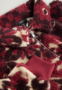 Bluza polarowa z zamkiem, z motywem kwiatowym w kolorach burgundu, kremowym i ciemnym brązie. Bordowe ściągacze na mankietach i kołnierzu. Miękka w dotyku.