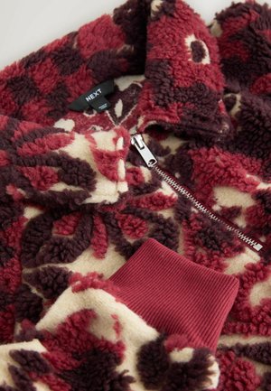 Fleecepullover med lynlås, med et blomstermønster i bordeaux, creme og mørkebrun. Ribstrikkede bordeaux ærmegab og krave. Blød tekstur.