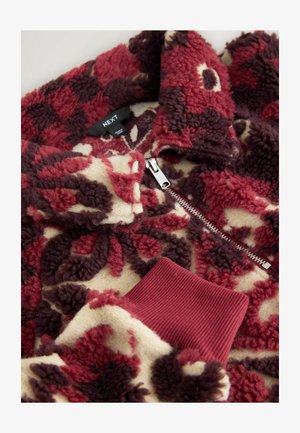 Fleecepullover med lynlås, med et blomstermønster i bordeaux, creme og mørkebrun. Ribstrikkede bordeaux ærmegab og krave. Blød tekstur.