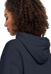 Felpa navy con finitura testurizzata, caratterizzata da un cappuccio con cordoncino e spalle scese, vista da dietro su capelli ricci.