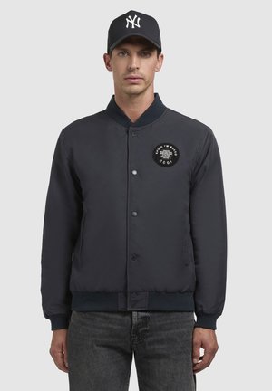Marineblauer Bomberjacke mit gerippten Bündchen und Kragen, Druckknopfverschluss und einem runden Aufnäher auf der Brust. Strukturierter Stoff, lässiges Design.