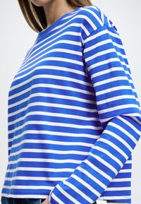 Modrá a biela pruhovaná dlhý rukáv tričko s okrúhlym výstrihom, s rovnomernými horizontálnymi pruhmi a voľným strihom. Jemná textúra látky.