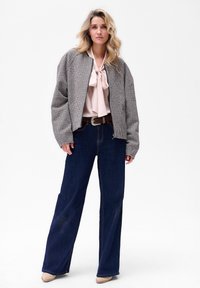 Kurtka bombowo-wzorzysta, różowa bluzka z krawatem, szerokie ciemnoniebieskie dżinsy, brązowy pasek, neutralne obuwie, gładka tekstura, luźny fason.