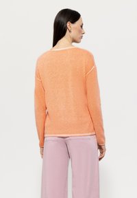 Light orange sweater with a soft texture, featuring white accent stitching along the neckline and hem. The design is relaxed fit with long sleeves.
