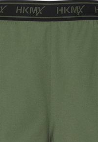 Gröna shorts med svart elastiskt midjeband med HKMX-logotyp. Slät textur utan synliga mönster eller detaljer. Enkel design.