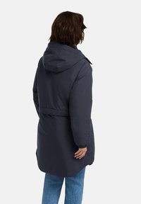 Cappotto imbottito blu navy scuro con cappuccio, caratterizzato da una vita regolata e polsini elasticizzati. Tessuto morbido, design lungo fino al ginocchio con una silhouette pratica.