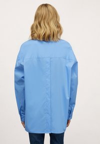 Light blue oversized button-up shirt made of smooth fabric, featuring a back seam, long sleeves, and a straight cut.