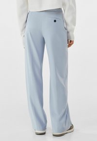 Light blue wide-leg trousers with a smooth texture, featuring a back pocket with a black button and a waistband. Footwear is grey.