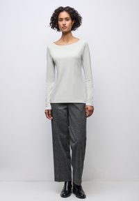 Haut à manches longues gris clair avec un large décolleté, associé à un pantalon à carreaux noirs et blancs à jambes larges et à des bottines noires.