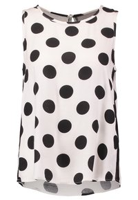 Haut sans manches en tissu blanc avec de grands pois noirs, encolure ronde et ourlet arrondi avec des fentes latérales pour faciliter les mouvements.