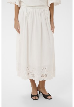 Vrouw draagt een witte midi-rok met een gegolfde, oogjeszoom en een geplooide taille, gecombineerd met zwarte open-toe kitten heel sandalen.