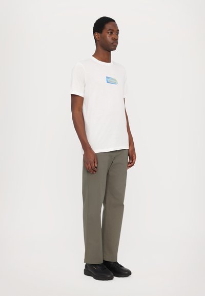 T-shirt blanche avec un graphisme multicolore sur le devant, associée à un pantalon vert olive et des chaussures noires. Design simple, coupe décontractée.