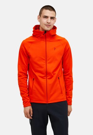 Lys orange zip-up jakke med høj krave, sidelommer og sorte lynlåsdetaljer. Stoffet ser glat og strækbart ud.