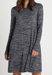 Robe à manches longues en marine foncé avec un motif texturé et chiné. Coupe décontractée avec un col arrondi et un subtil drapé sur les côtés.