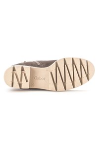 Zapato de ante marrón con una suela texturizada, que presenta un patrón zigzagueante y una marca. La suela exterior es beige con surcos de tracción pronunciados.