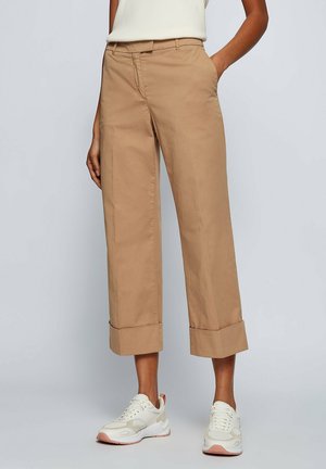 Kvinde iført beige cropped vidde bukser med høj talje og opbukket kant, kombineret med hvide sneakers og en hvid top, der er stukket ind.