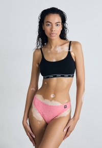 Black crop top with logo band and pink lace hipster panties featuring scalloped edges. Smooth fabric textures and contrasting colors.