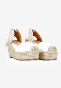 Cuñas blancas de esparto con plataforma de yute, punta redonda y tira trasera de malla beige. Presentan un tacón envuelto y detalle de lazada en el tobillo.