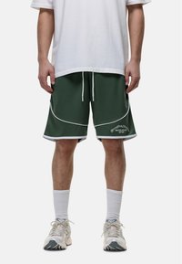 Groene sportshorts met witte bies, een elastische tailleband en een logo op het linkerbeen. Draag met een wit shirt en lichte sneakers.