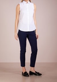Bílá bezrukávová košile s knoflíky, námořnické slim-fit kalhoty a černé mokasíny. Materiál vypadá hladce, s klasickým designem límečku.