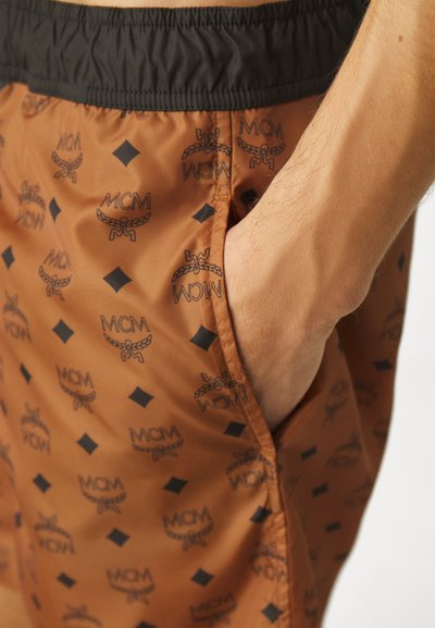 Pantaloni scurți de înot maro cu talie elastică neagră, având un model repetitiv cu logo și accente mici de diamant, făcuți dintr-un material neted.