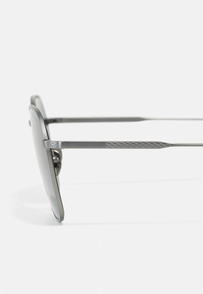Ochelari de soare din metal cu un cadru gri, având detalii texturate pe temple și lentile întunecate. Design minimalist.