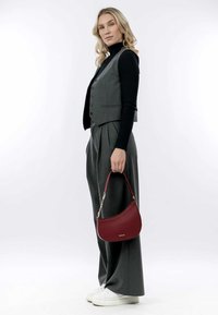 Gilet grigio su un dolcevita nero, abbinato a pantaloni grigi a vita alta e una borsa bordeaux strutturata con una forma curva.
