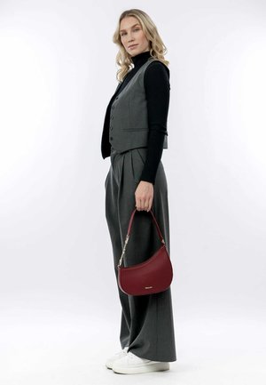 Gilet grigio su un dolcevita nero, abbinato a pantaloni grigi a vita alta e una borsa bordeaux strutturata con una forma curva.
