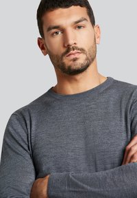 Grauer Rundhalsausschnitt-Pullover aus strukturiertem Strickstoff. Figurbetonter Schnitt mit langen Ärmeln und gerippten Bündchen. Sauberes, minimalistisches Erscheinungsbild.