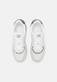 White sneakers with a textured leather upper, contrasting grey accents on the heel, flat white laces, and a small perforated pattern on the toe.