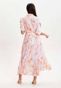 Long dress in lightweight fabric, featuring a white and orange tie-dye pattern, ruffled accents, and a fitted waist with a flared hem.