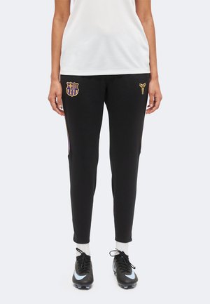 Pantalon de sport noir slim avec logos dorés FC Barcelone et Kobe Bryant, porté avec des chaussettes blanches et des chaussures de football noires Nike.
