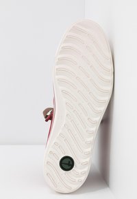 Czerwony tenis z teksturowaną gumową podeszwą. Posiada brązowy materiałowy pasek i czarne okrągłe logo. Czysty, minimalistyczny design z płaskim profilem.