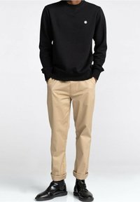 Sweat-shirt noir à col rond avec des poignets côtelés, associé à un chino beige clair et des bottines noires. Pantalon avec devant plat et ourlets retroussés.