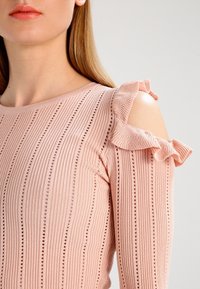 Top a costine rosa chiaro, con maniche scoperte decorate da volant e piccoli dettagli a taglio lungo linee verticali.