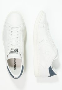 Baskets en cuir blanc à texture lisse, design à lacets, accents discrets en forme d'étoile, et détails en daim gris au talon.