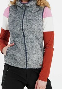 Graues Kunstfell-Westen mit hohem Kragen, Reißverschluss und seitlichen Taschen. Getragen über einem mehrfarbigen Langarmshirt mit glatter Textur.