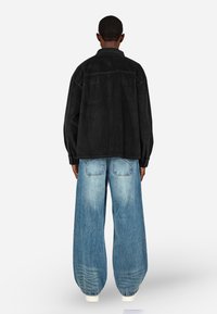 Czarna ekoskórzana oversize kurtka z kołnierzem, zestawiona z jasnoniebieskimi szerokimi dżinsami. Widoczne przeszycia i dwie tylne kieszenie.